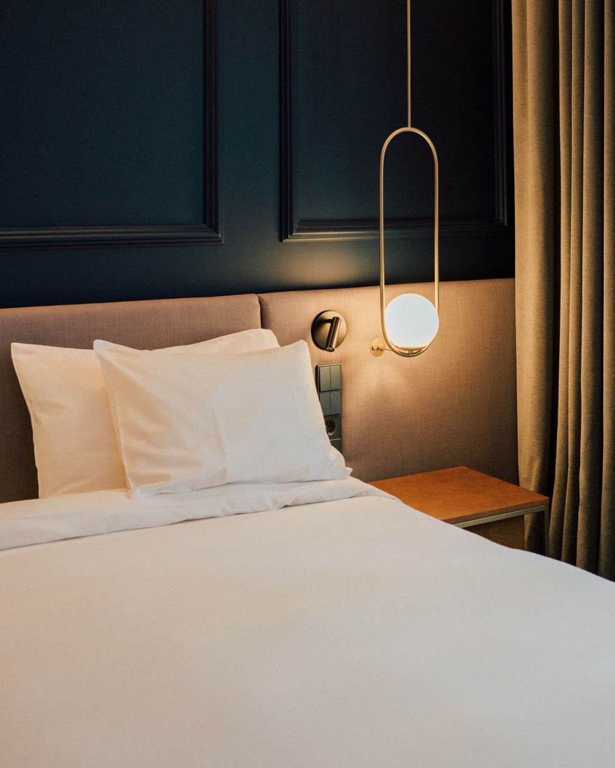 Lit aux draps blancs, tête de lit capitonnée et suspension en laiton sur un mur bleu nuit